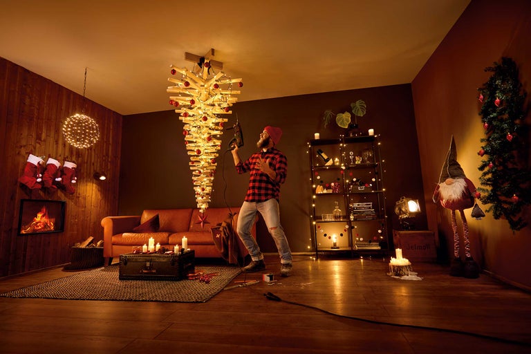 Living cu brad de Crăciun modern din lemn, iluminat și decorat cu globuri roșii, bărbat cu mașină de găurit