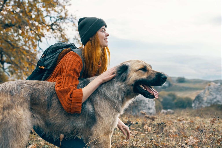 Femeie care mângâie un câine în natură cu un rucsac și o căciulă