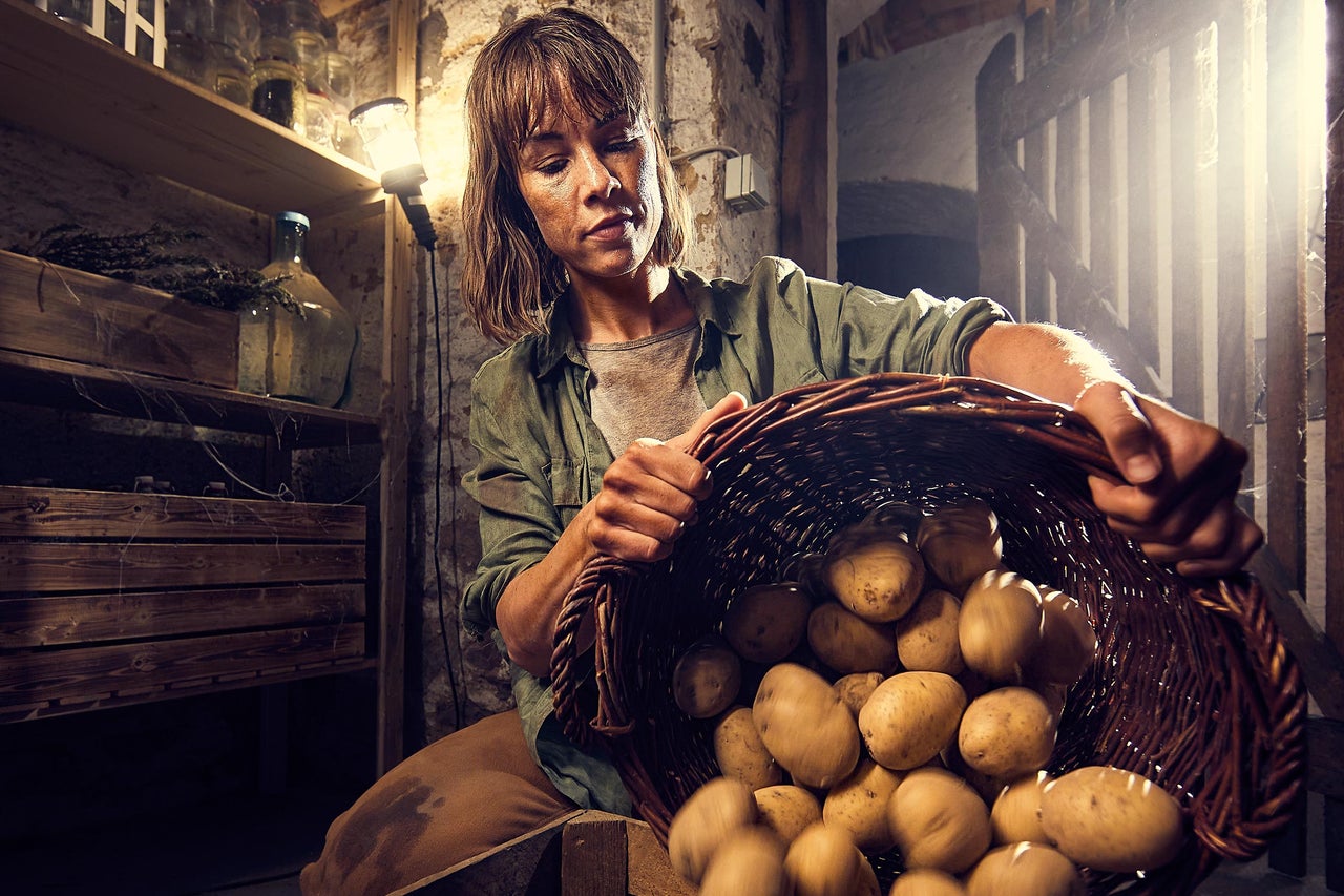 Femeie ține un coș cu cartofi în pivniță.