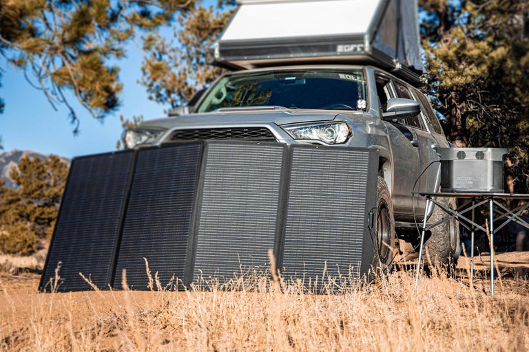 Fotografie cu un vehicul de teren argintiu cu modul solar și stație de alimentare portabilă în natură.