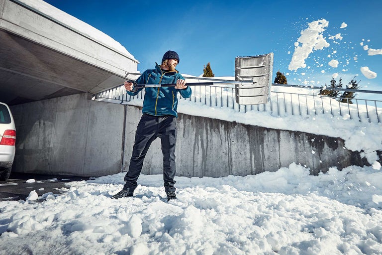 Bărbat care curăță zăpada cu o lopată de zăpadă în fața unui zid de beton