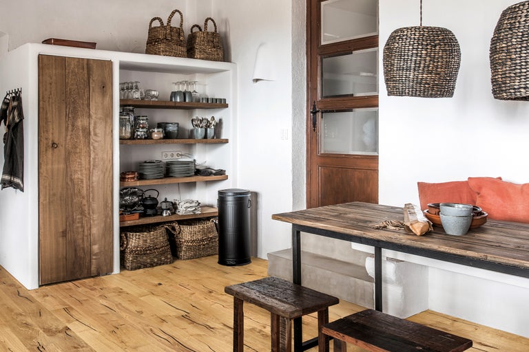 Scenă de bucătărie cu masă din lemn, scaune, rafturi, dulapuri și elemente decorative