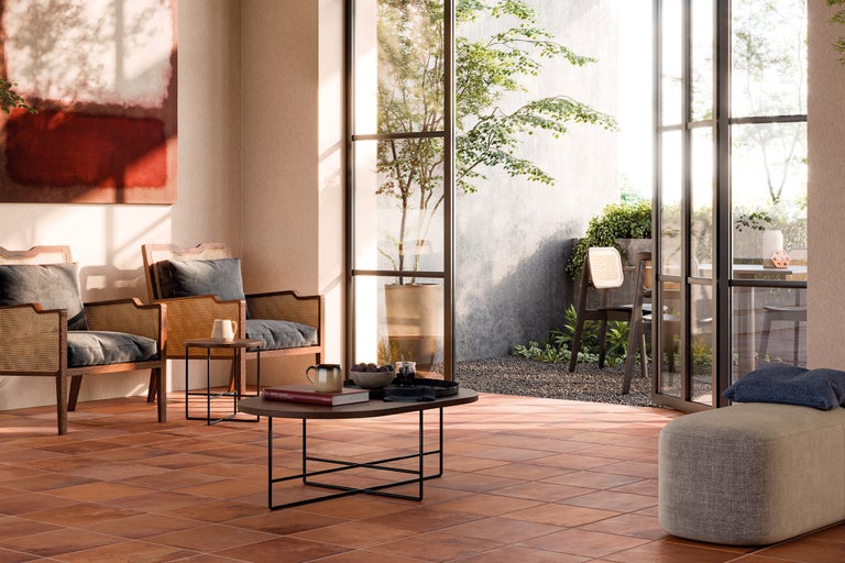 Living luminos cu gresie de teracotă, fotolii din ratan și vedere spre grădină