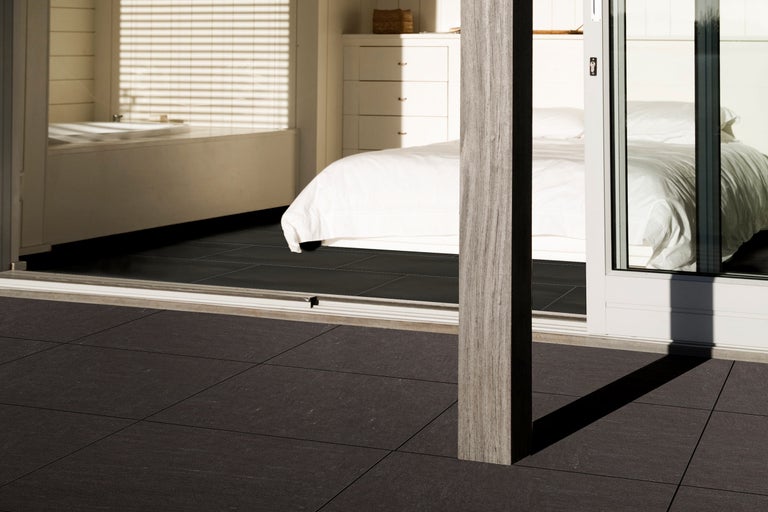 Terasa cu plăci închise la culoare, vedere spre un dormitor cu pat și baie