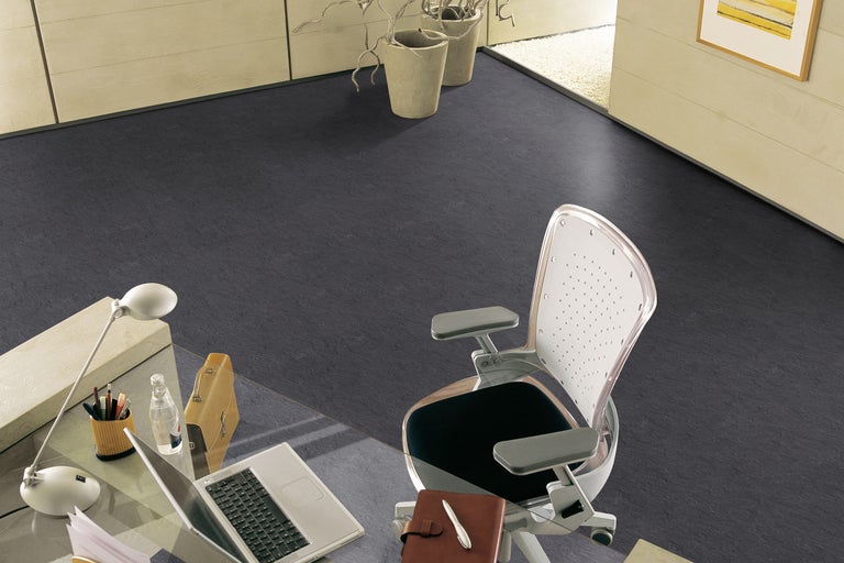 Spațiu de birou cu pardoseală închisă la culoare, birou și scaun de birou