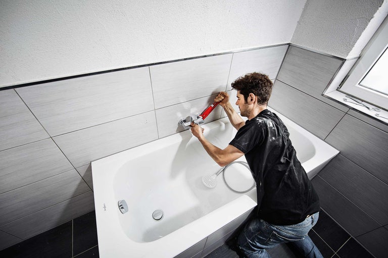 Instalator montează bateria de baie în baie cu gresie