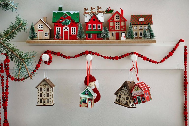 Ornamente decorative din lemn, în formă de căsuțe, cu ghirlandă de mărgele roșii pe un raft