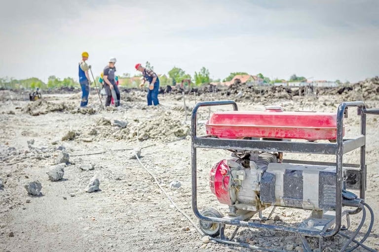 Generator de curent mobil pe un șantier cu muncitori în fundal.
