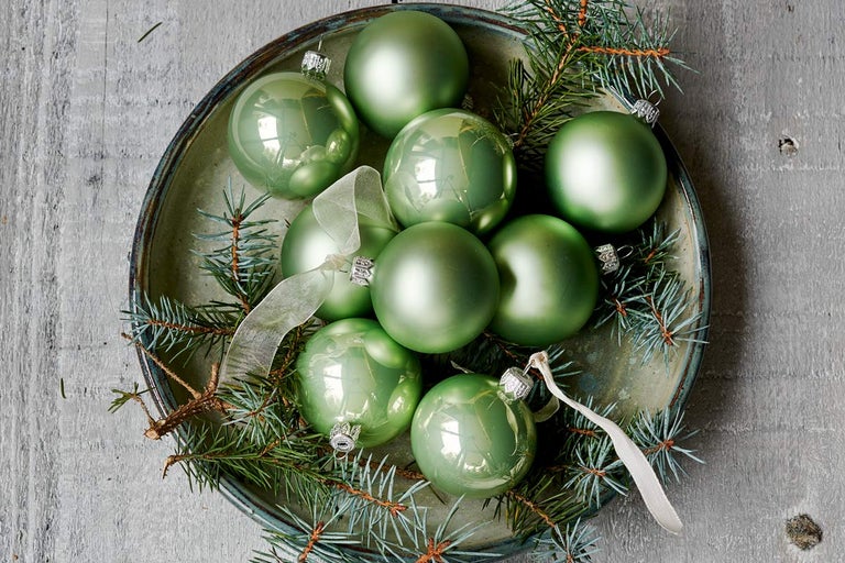 Globuri verzi de Crăciun într-un vas cu ramuri de brad și panglici