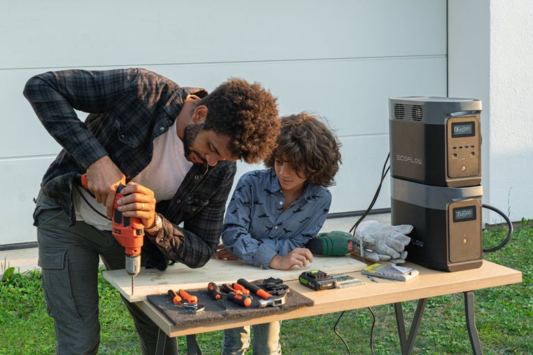 Un tată și fiul său dau o gaură într-o scândură pe o masă, cu centrală electrică EcoFlow