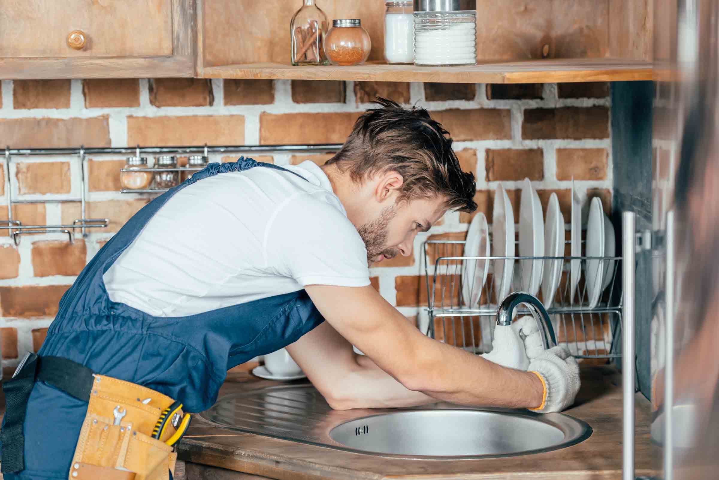Instalator care lucrează la o chiuvetă într-o bucătărie