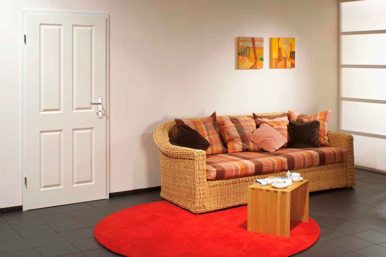 Living cu ușă de interior, canapea din ratan și covor roșu