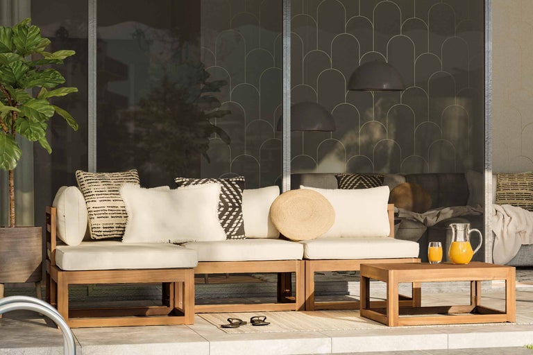 Zonă de living în aer liber cu mobilier din lemn, perne și măsuță laterală cu băuturi