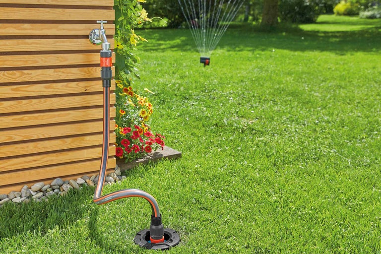 Scenă de grădină cu robinet, racord de furtun, furtun de grădină și aspersor de gazon