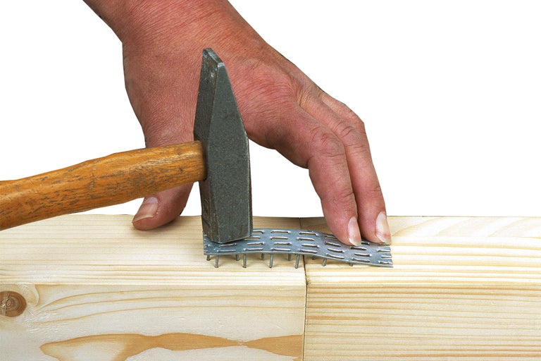 Un ciocan bate o placă de cuie în două bucăți de lemn.