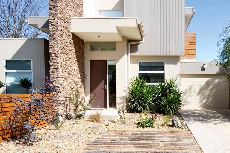 Exteriorul unei case moderne cu fațadă de piatră, gard din lemn și amenajare peisagistică