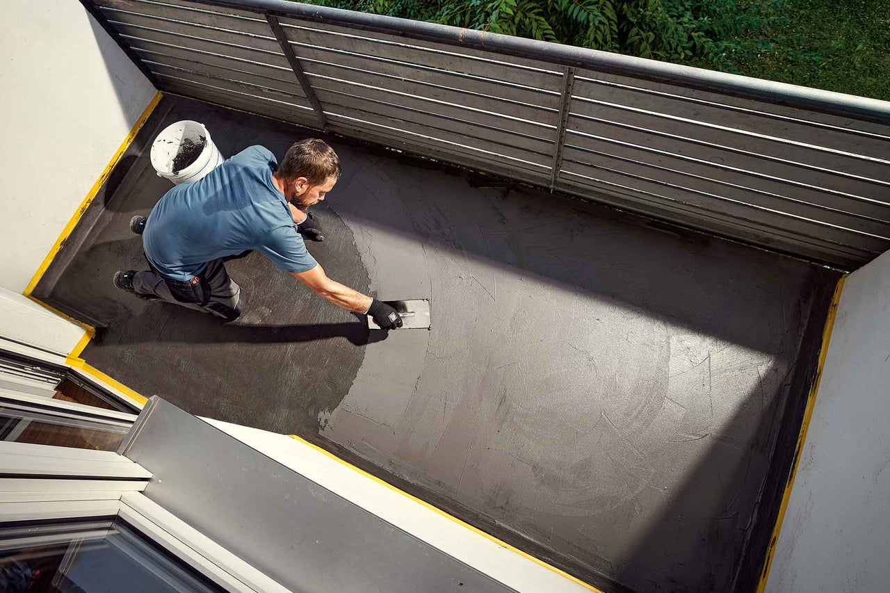 Un bărbat aplică un strat gri cu o mistrie pe un balcon