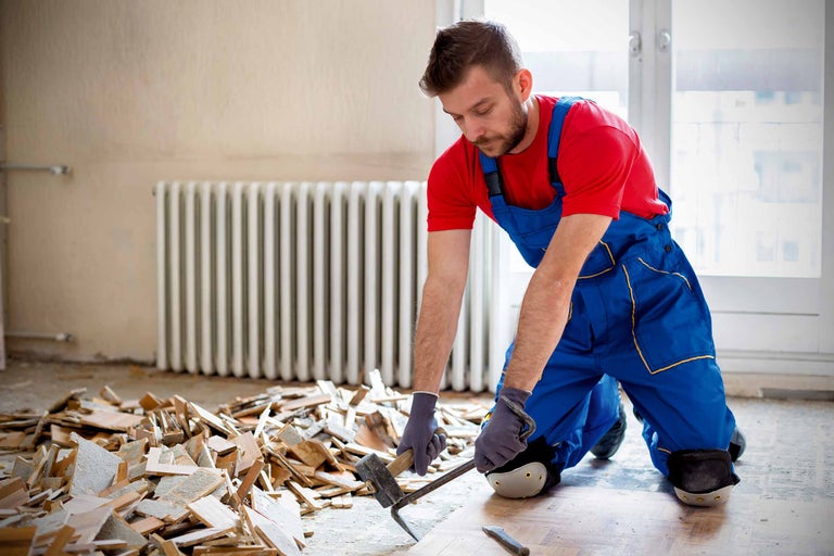 Muncitor îndepărtând plăci vechi de podea cu un ciocan și o daltă