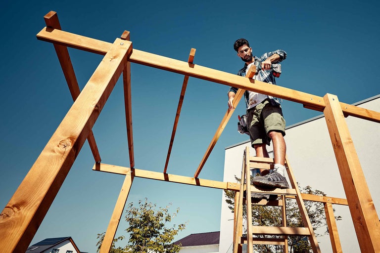 Un meșter montează o construcție din lemn cu o șurubelniță cu acumulator în grădină.