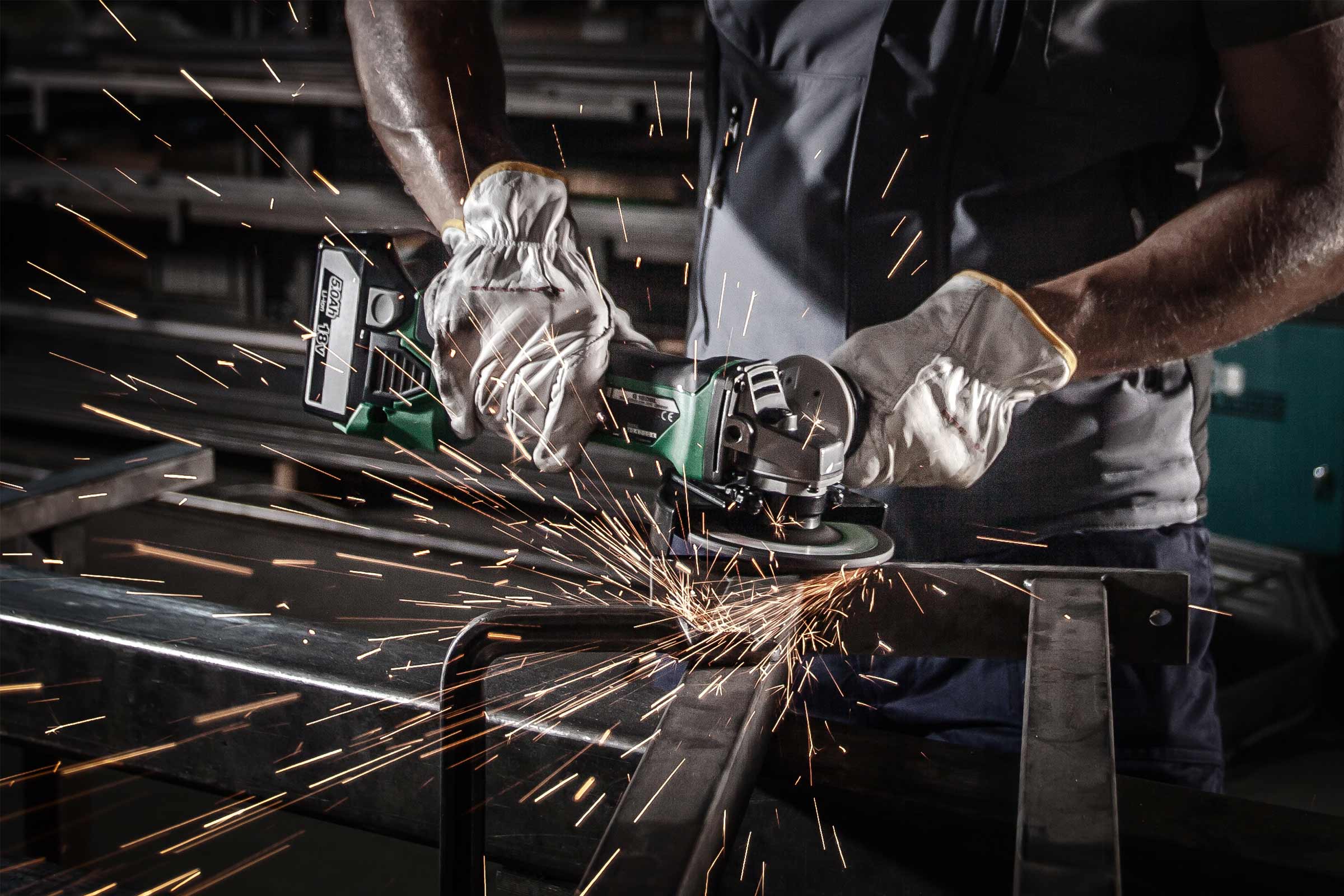 O persoană folosește un polizor unghiular pentru a tăia metal, producând scântei.