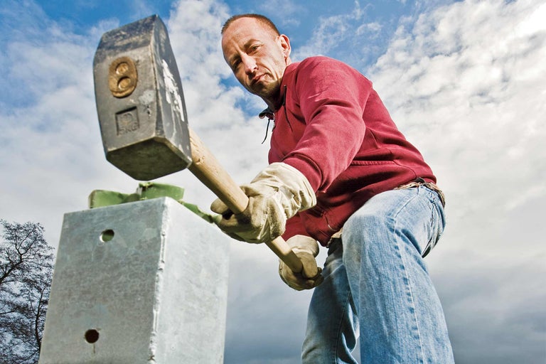 Bărbat cu barosul bătând un stâlp metalic