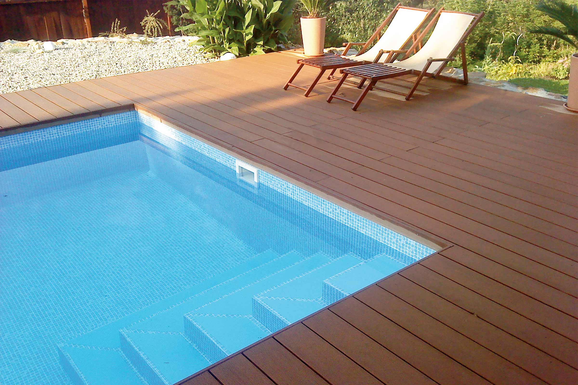 Piscină cu gresie mozaic și terasă din lemn cu șezlonguri