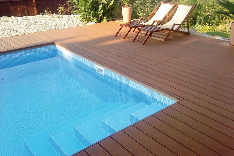 Piscină cu gresie mozaic și terasă din lemn cu șezlonguri