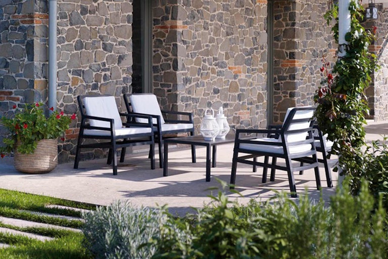 Set de mobilier de grădină cu masă și scaune pe terasă în fața unui zid de piatră