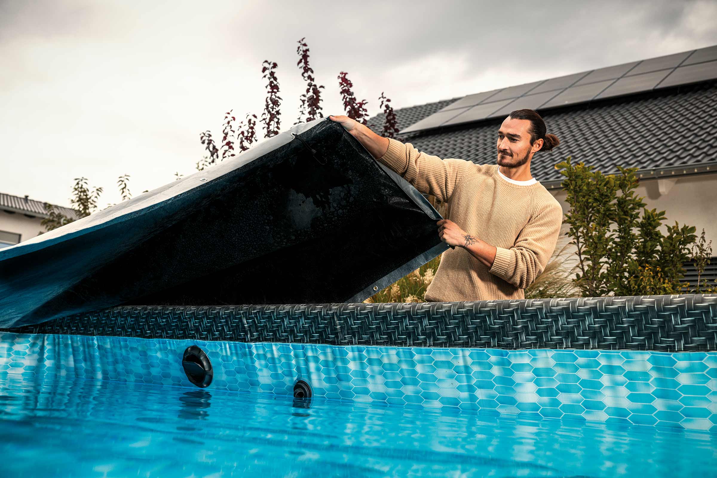 Bărbat îndepărtând prelata piscinei de pe piscina supraterană din grădină
