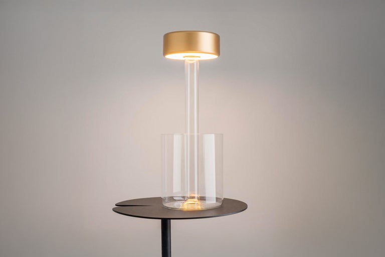 Lampă de masă cu cilindru din sticlă transparentă pe o măsuță laterală