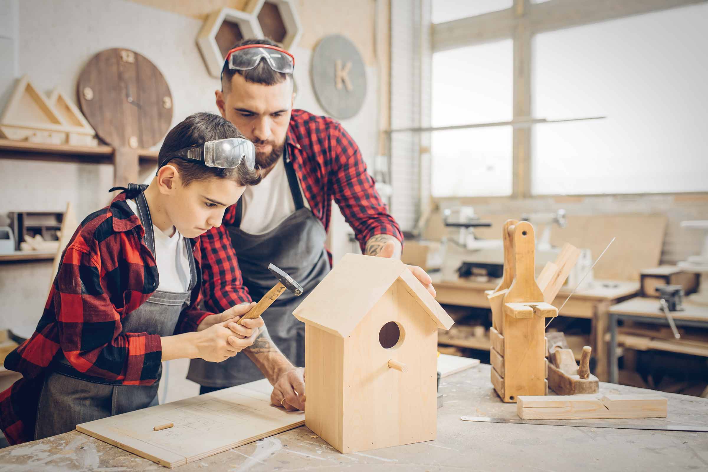 Tată și fiu construiesc împreună o căsuță pentru păsări în atelier.