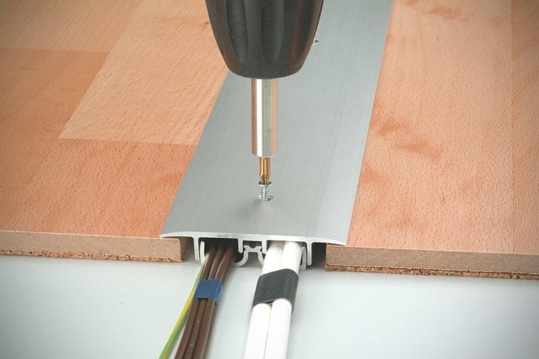 Fixarea unei plinte de protecție a cablurilor din aluminiu pe o podea de lemn cu o șurubelniță