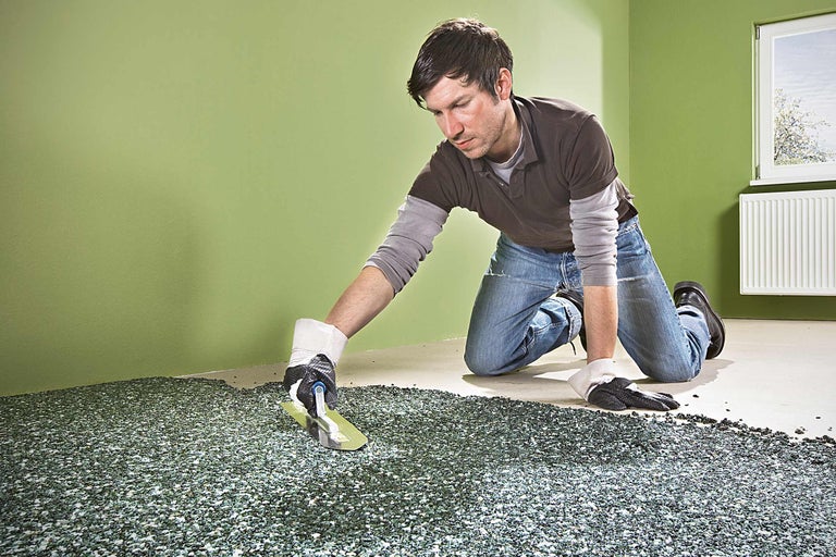 Un bărbat așază un covor de piatră cu o mistrie într-o cameră.