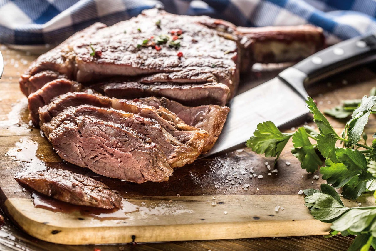 Friptură Tomahawk, feliată, pe scândură de lemn cu cuțit și pătrunjel