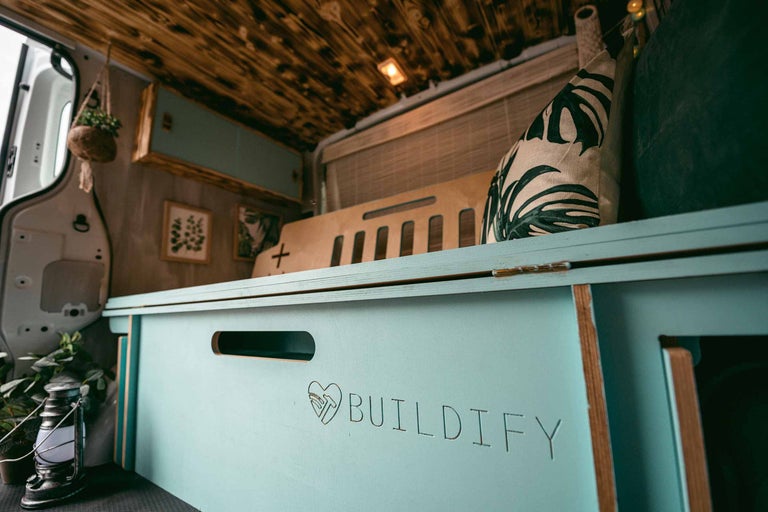 Interiorul unei autoutilitare transformate cu plafon din lemn, dulapuri de culoarea mentei, perne decorative și inscripția Buildify