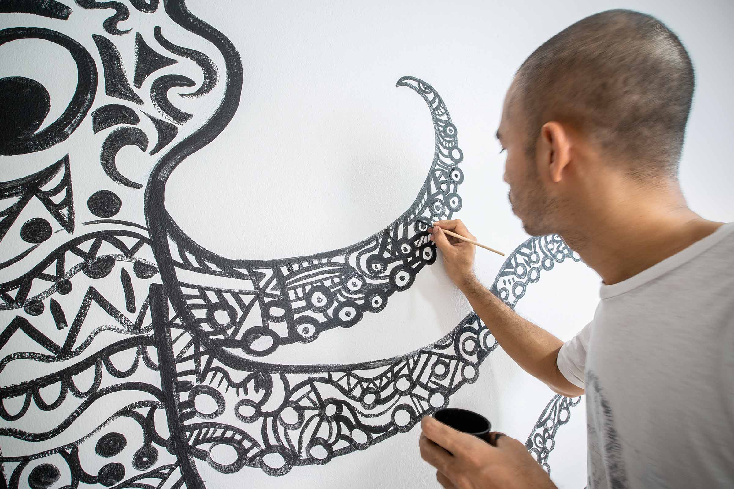 Un artist pictează un model abstract pe un perete cu o pensulă.