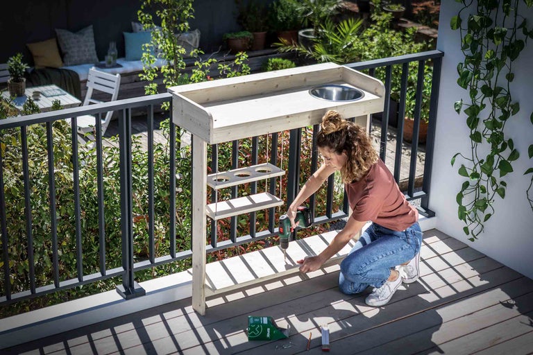 Femeie asamblând o masă de grădină cu chiuvetă pe un balcon.