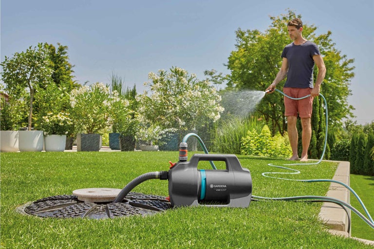Scenă de grădină cu un bărbat udând plante cu o pompă de grădină Gardena