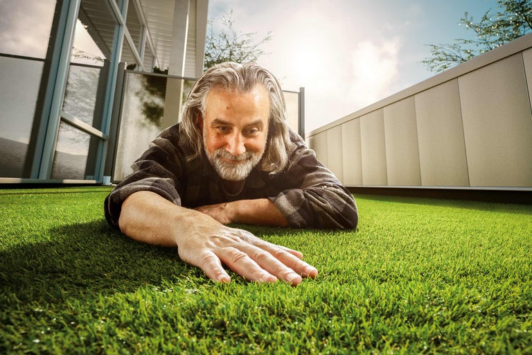 Un bărbat stă întins pe gazon artificial și îl atinge cu mâna