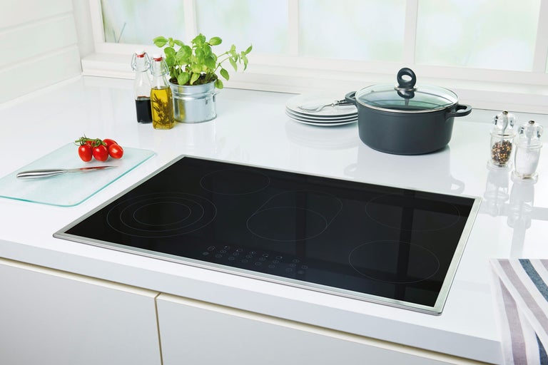 Plită cu inducție neagră cu cinci zone de gătit pe un blat de bucătărie.