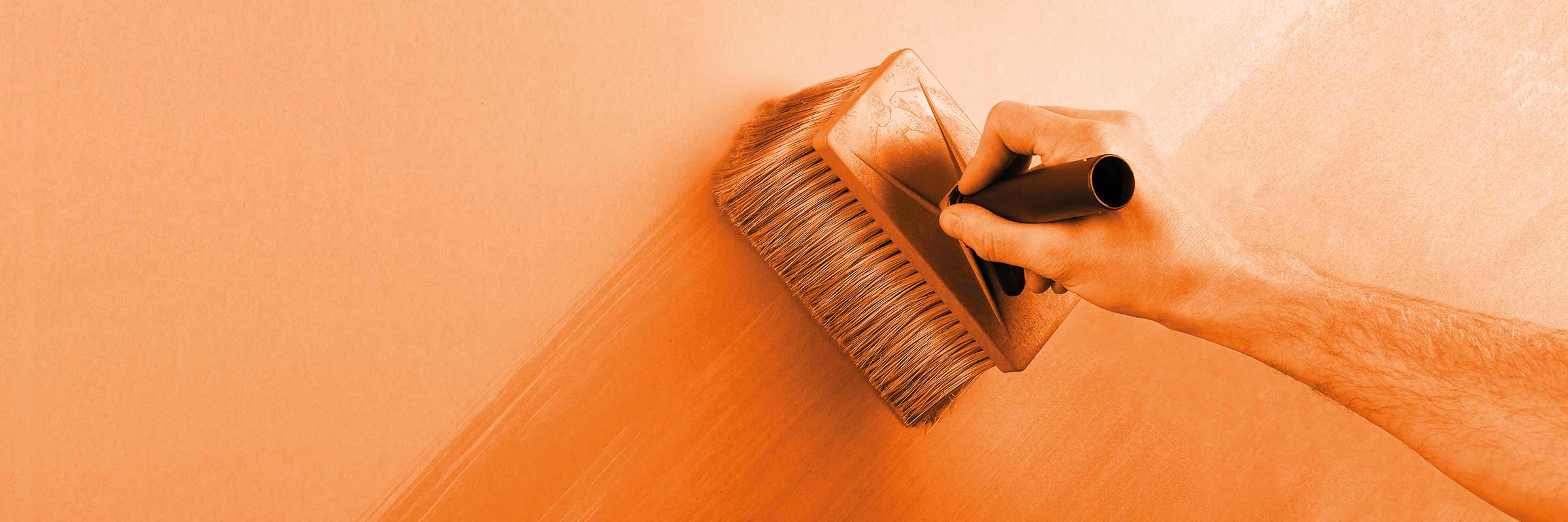 O persoană aplică o perie de lazură pe un perete