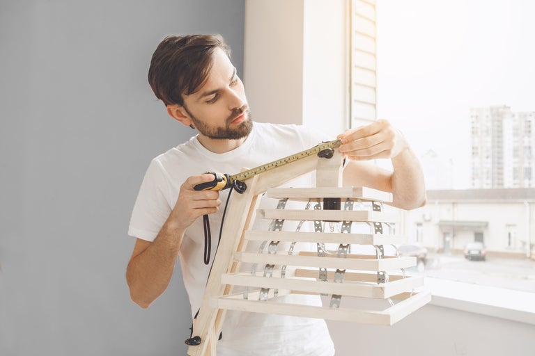 Un bărbat măsoară o lampă de lemn cu o ruletă.