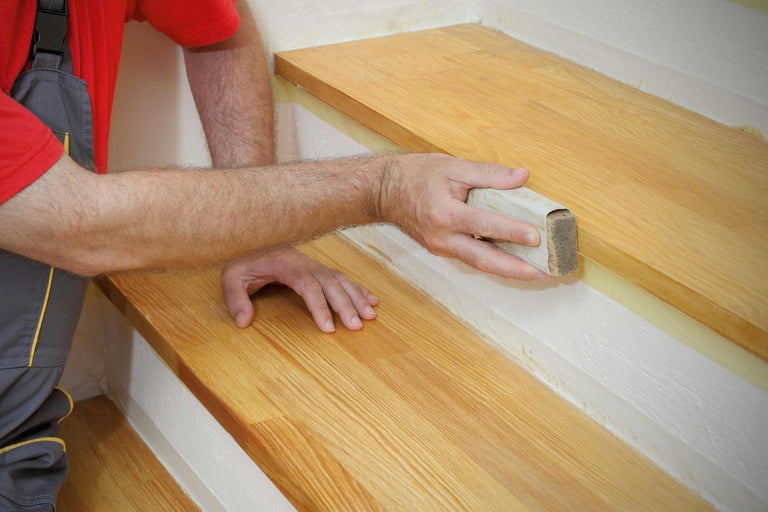 Artizan care lucrează o scară din lemn cu un bloc de șlefuit