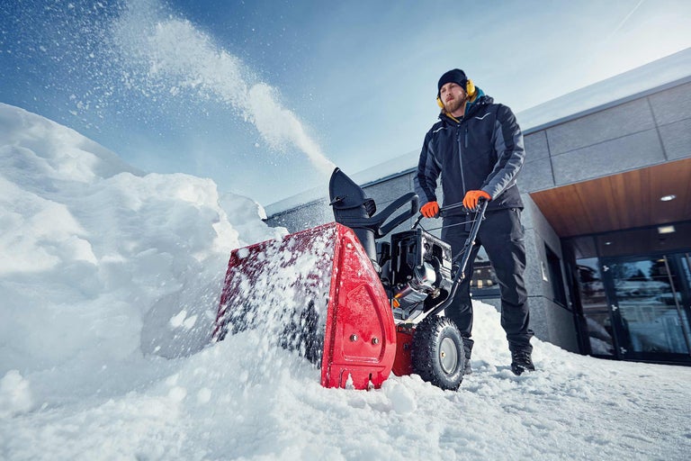 Bărbat folosește o freză de zăpadă pentru a curăța zăpada din fața clădirii