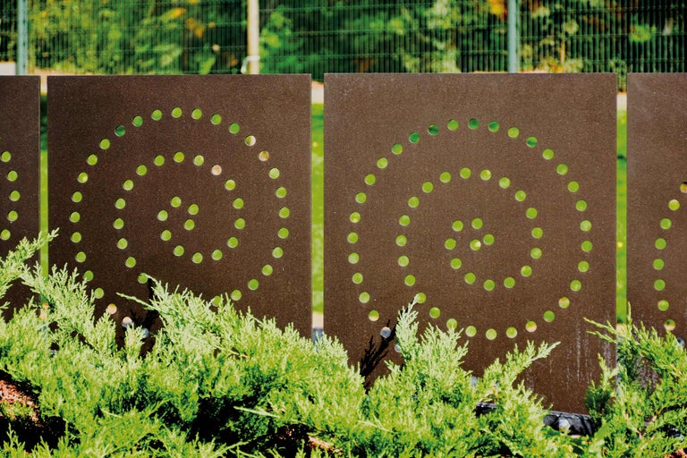 Elemente decorative de gard metalice cu model perforat circular și plante verzi