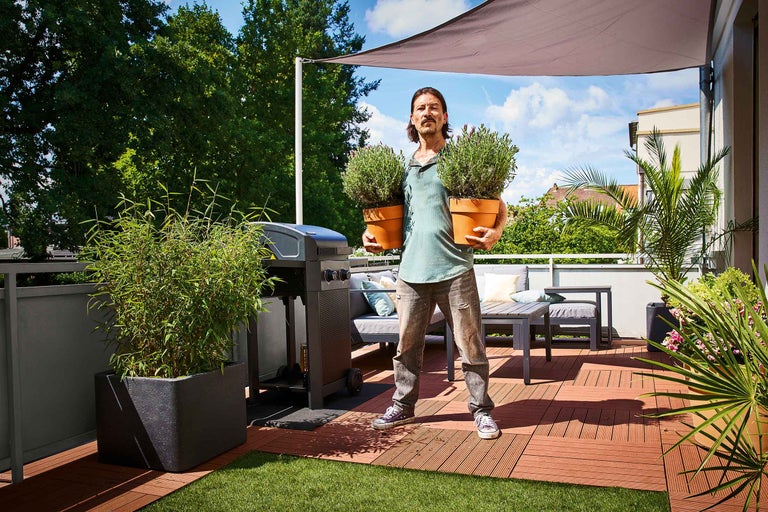 Femeie care asamblează o jardinieră mobilă din lemn pe un balcon cu unelte și plante.