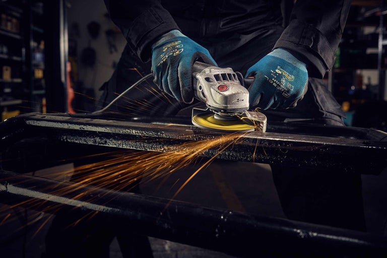 Bărbat cu mănuși șlefuind metal cu un polizor unghiular, sar scântei