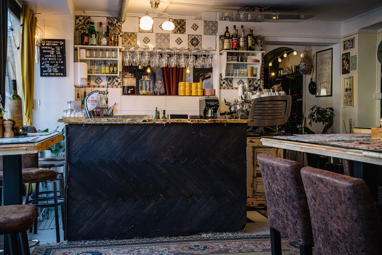 Interiorul unei cafenele cu bar, rafturi și mese.
