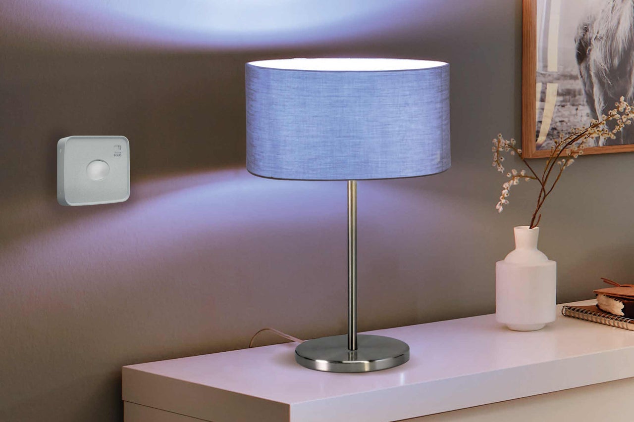 Lampă de masă decorativă cu abajur din material textil și întrerupător de perete asortat pentru a controla iluminatul.