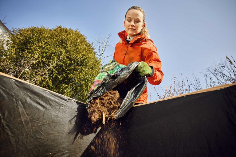 Femeie care toarnă pământ dintr-un sac într-un strat de grădină ridicat